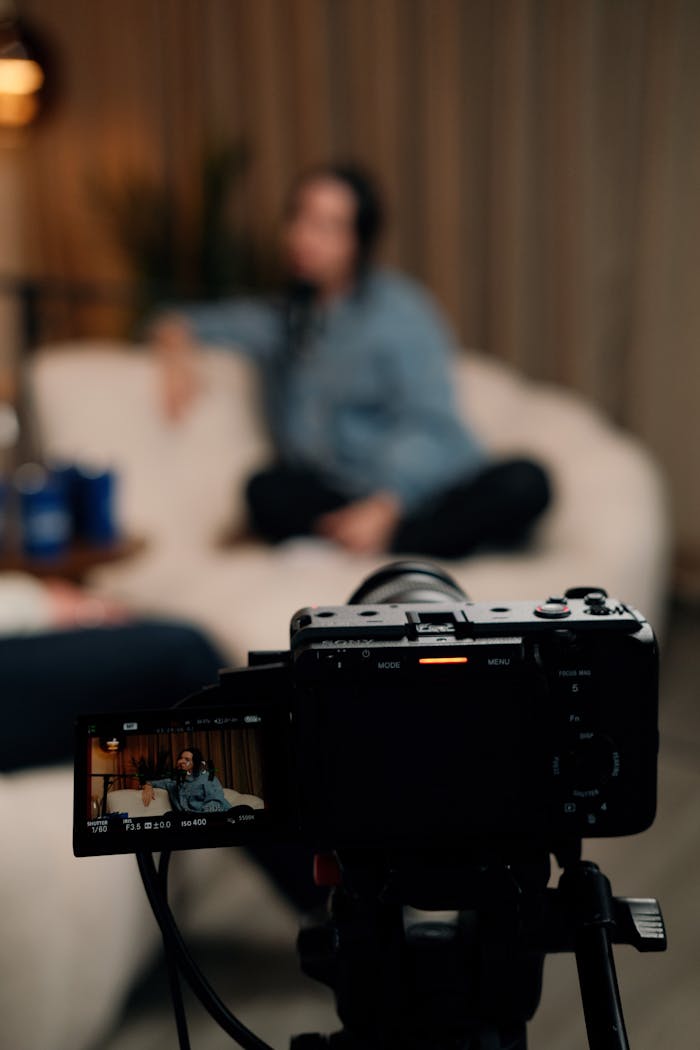 A podcast recording session with a camera capturing a speaker on a sofa indoors.