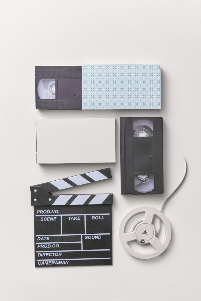 Flat lay of vintage video equipment including cassettes and clapperboard on white backdrop.
